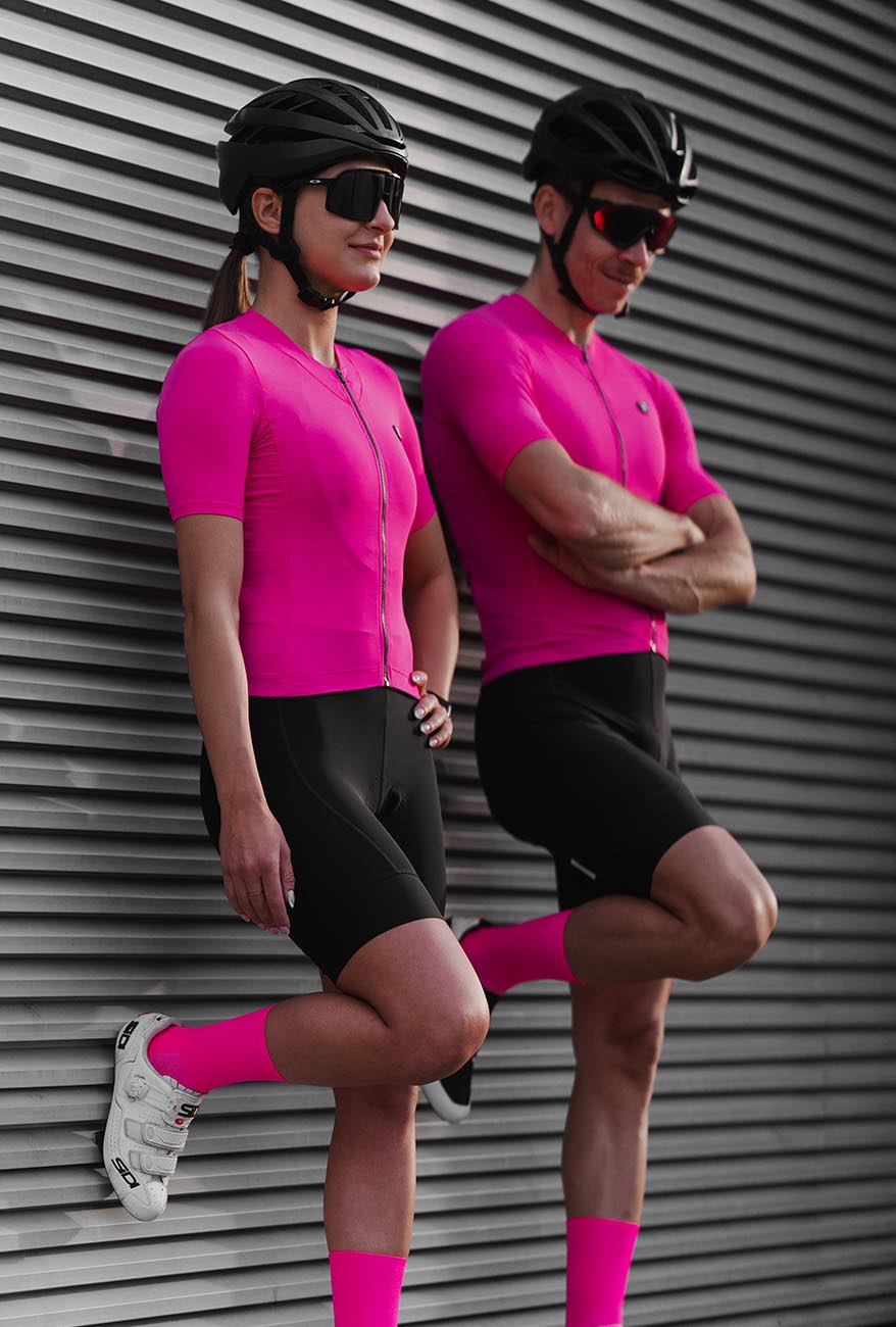 women and men standing next to wall and are wearing pink cycling outfit for road and gravel cyclists